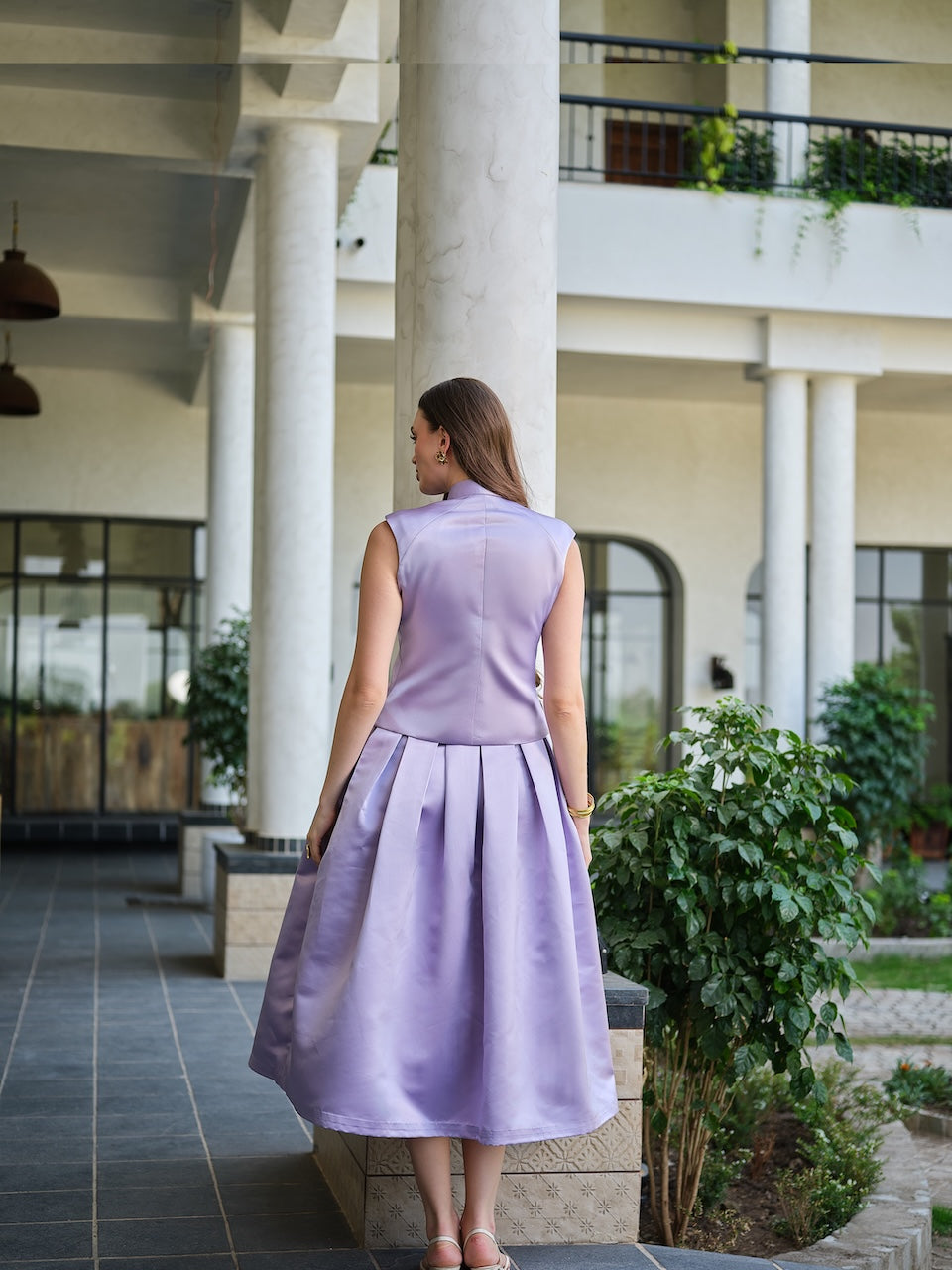 VIRELLE- A lavender sleeveless jacket with metal floral buttons paired with a box pleat skirt.