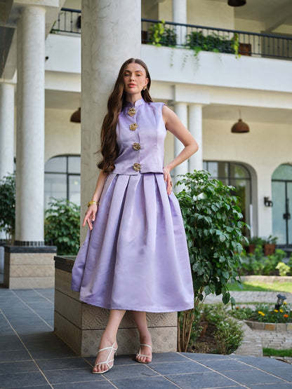 VIRELLE- A lavender sleeveless jacket with metal floral buttons paired with a box pleat skirt.