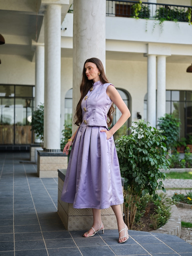 VIRELLE- A lavender sleeveless jacket with metal floral buttons paired with a box pleat skirt.