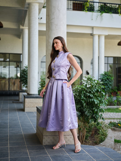 VIRELLE- A lavender sleeveless jacket with metal floral buttons paired with a box pleat skirt.