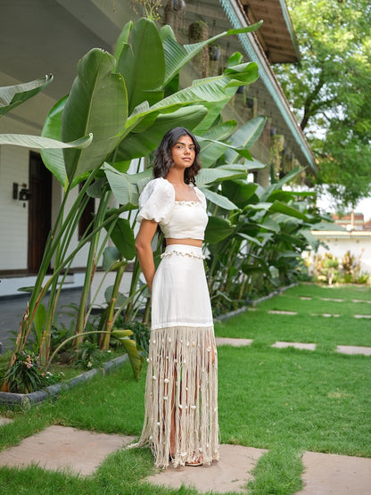 LAVIQUE - An ivory pleated co-ord with floral detailing and a tasseled skirt.